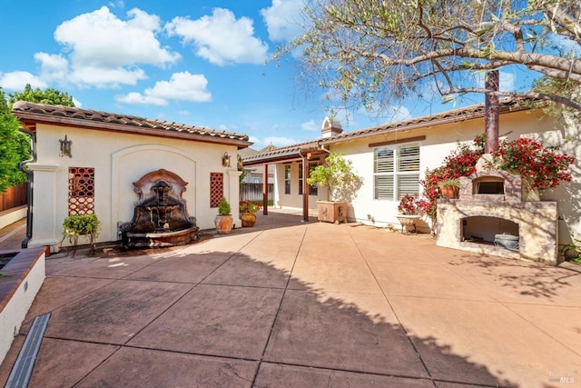 rear view of property with a chimney, a patio, stucco siding, and an outdoor fireplace