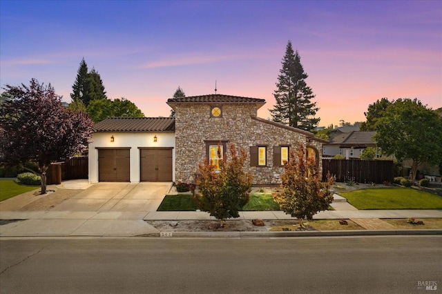 mediterranean / spanish-style home featuring concrete driveway, stone siding, a garage, and fence