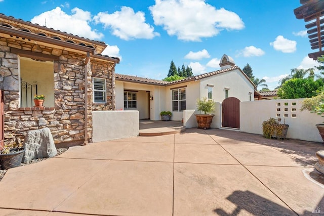 view of front facade featuring stone siding, a patio area, a tile roof, and a gate