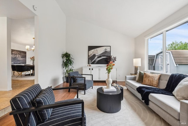 living area with baseboards, an inviting chandelier, wood finished floors, and vaulted ceiling
