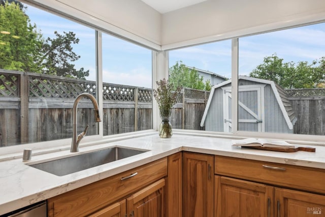 kitchen with light stone counters, brown cabinetry, and a sink