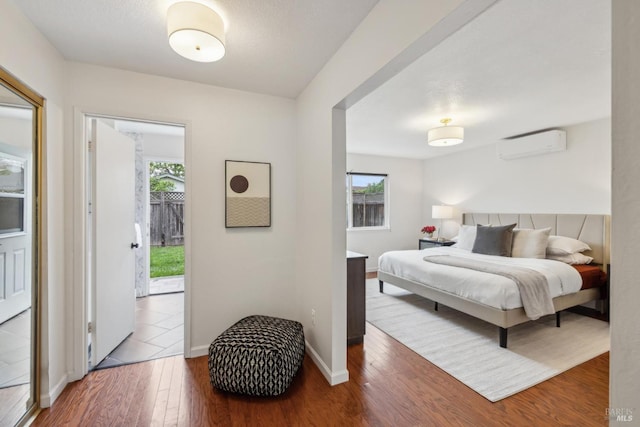 bedroom featuring baseboards, a wall mounted air conditioner, wood finished floors, and multiple windows
