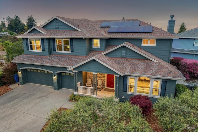view of front of property featuring concrete driveway, an attached garage, solar panels, and covered porch