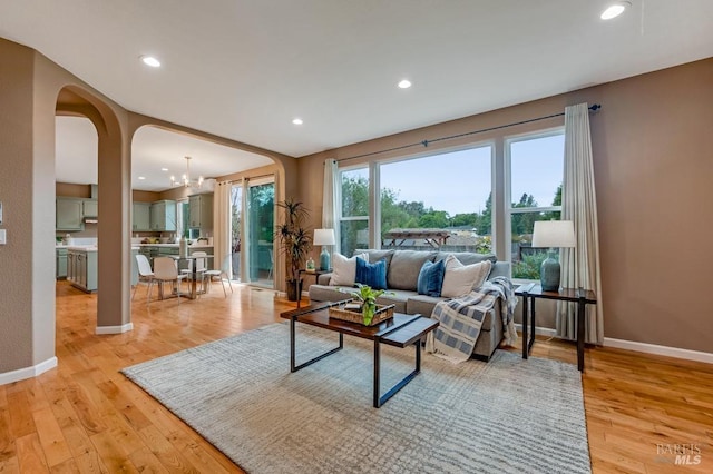 living room with arched walkways, baseboards, recessed lighting, and light wood-type flooring