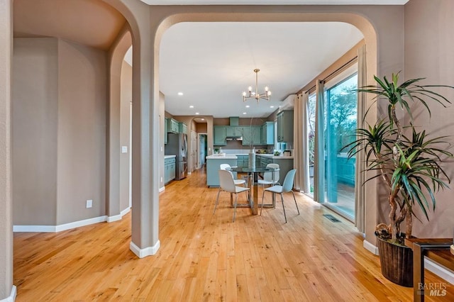 dining area with an inviting chandelier, arched walkways, and light wood finished floors