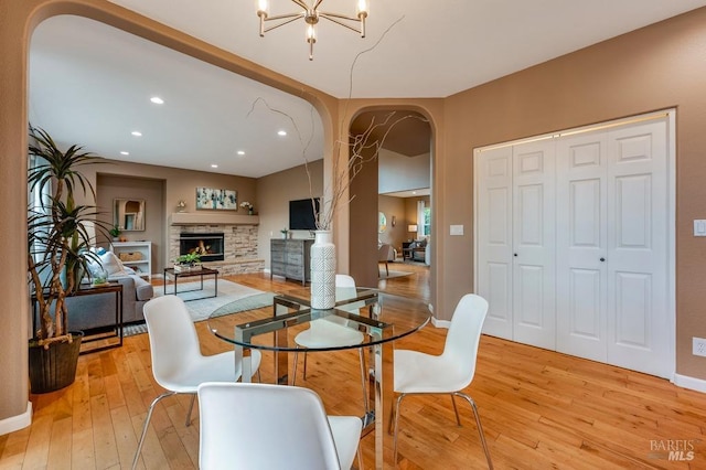dining area featuring a warm lit fireplace, recessed lighting, arched walkways, light wood finished floors, and a notable chandelier