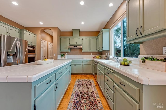 kitchen featuring appliances with stainless steel finishes, light wood-type flooring, a sink, green cabinetry, and recessed lighting