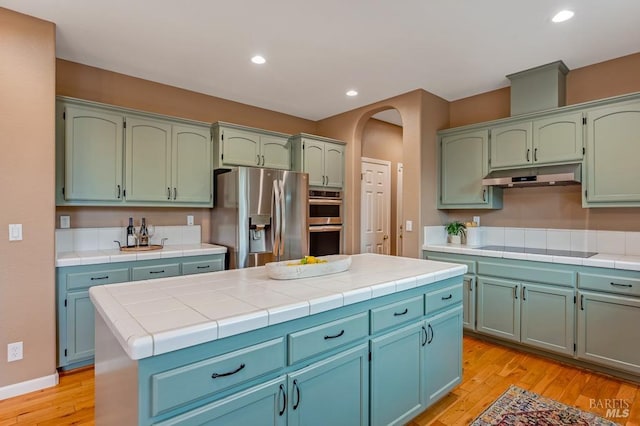 kitchen featuring under cabinet range hood, tile countertops, appliances with stainless steel finishes, and light wood-type flooring