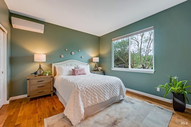 bedroom with baseboards, a wall mounted air conditioner, and wood finished floors