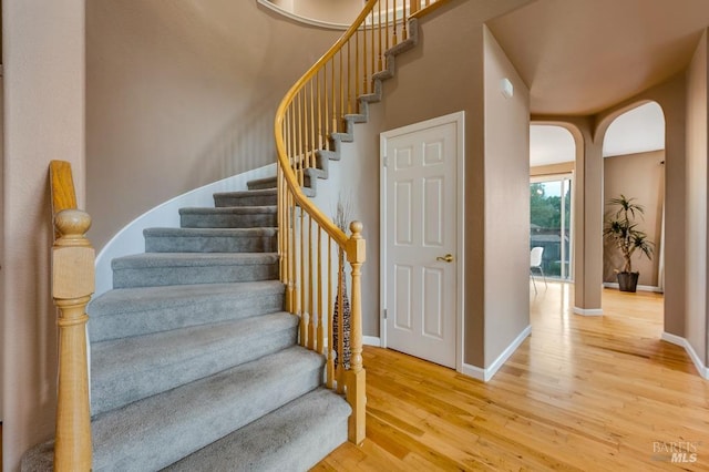 stairs featuring arched walkways, baseboards, and wood finished floors