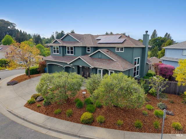 view of front of property with fence, a chimney, a shingled roof, roof mounted solar panels, and concrete driveway