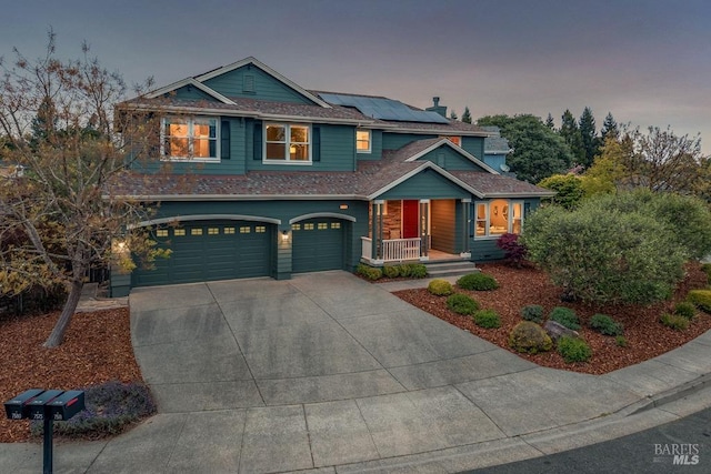 craftsman house with covered porch, solar panels, roof with shingles, a garage, and concrete driveway