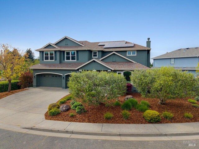 view of front of home featuring an attached garage, roof mounted solar panels, and driveway