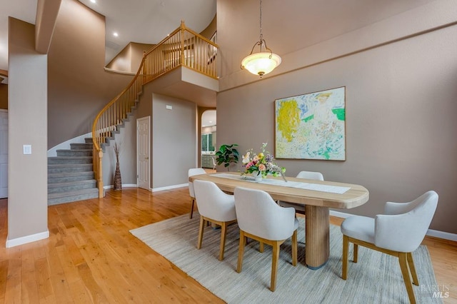 dining room featuring stairs, baseboards, wood finished floors, and a high ceiling
