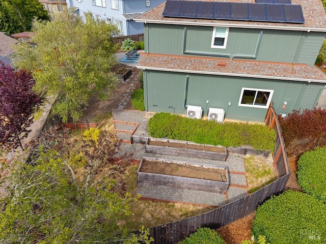 rear view of property with a shingled roof, ac unit, a vegetable garden, roof mounted solar panels, and a fenced backyard