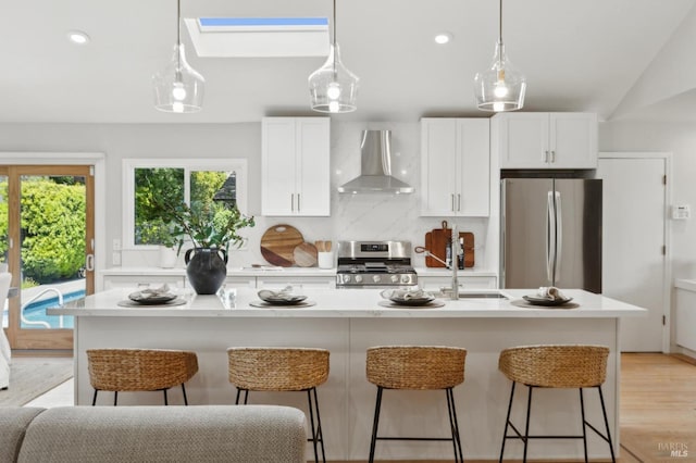 kitchen featuring wall chimney range hood, a kitchen bar, light countertops, white cabinetry, and stainless steel appliances