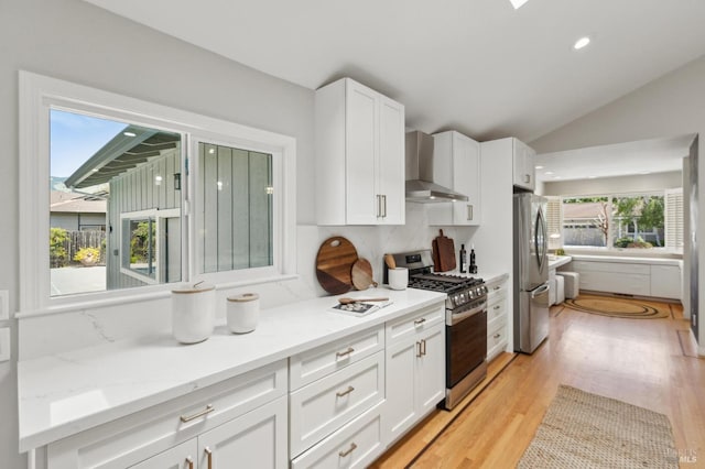 kitchen featuring lofted ceiling, light wood-style floors, wall chimney range hood, white cabinetry, and stainless steel appliances