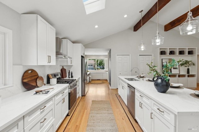 kitchen featuring wall chimney range hood, white cabinets, a sink, light wood-style flooring, and appliances with stainless steel finishes