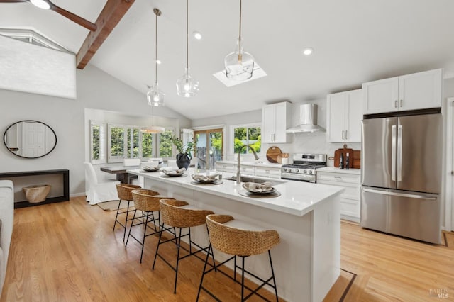 kitchen with beamed ceiling, a breakfast bar area, wall chimney exhaust hood, a sink, and stainless steel appliances