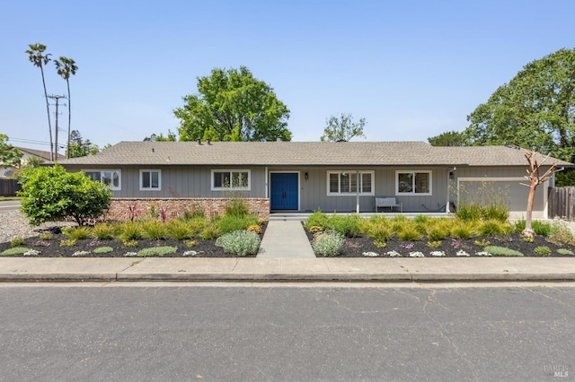 ranch-style home featuring brick siding, an attached garage, and roof with shingles