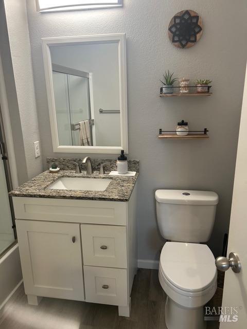 bathroom featuring a shower with shower door, wood finished floors, vanity, baseboards, and toilet