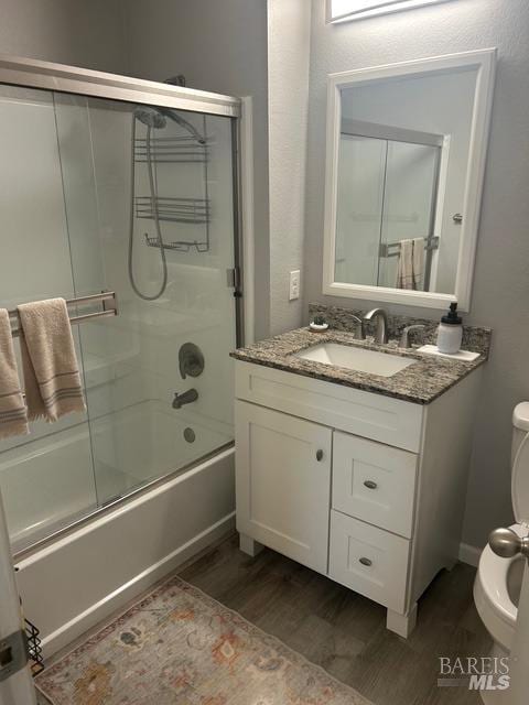 bathroom with bath / shower combo with glass door, vanity, toilet, and wood finished floors