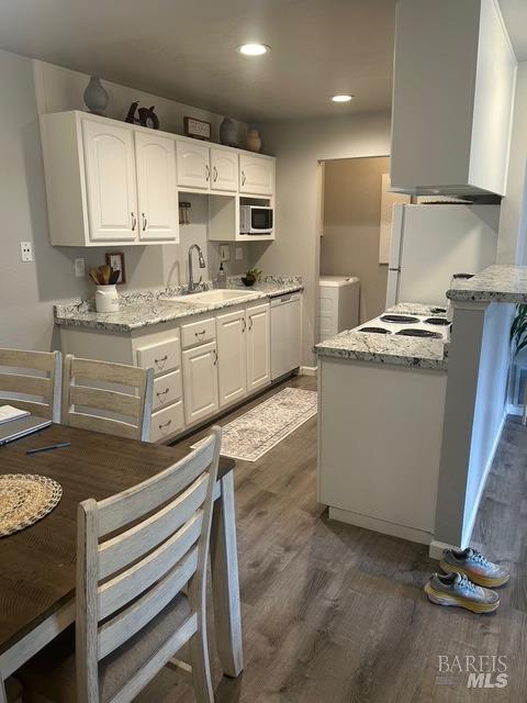 kitchen with freestanding refrigerator, dark wood-style flooring, white cabinets, washing machine and clothes dryer, and a sink
