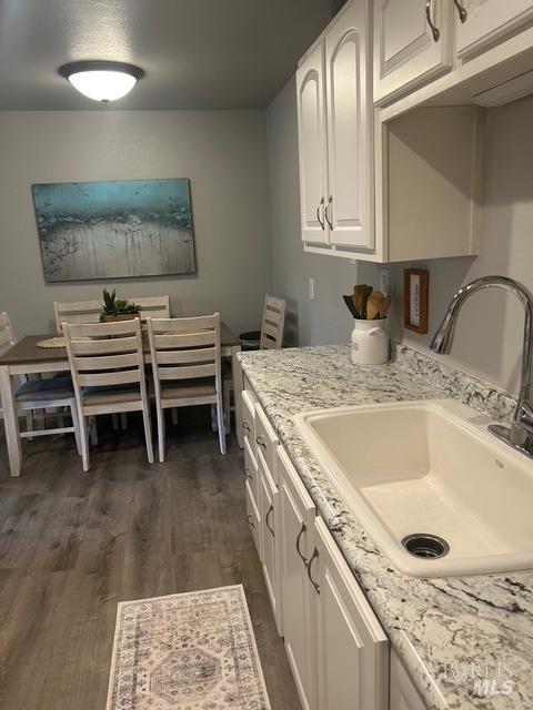 kitchen featuring light stone countertops, dark wood finished floors, dishwasher, a sink, and white cabinets