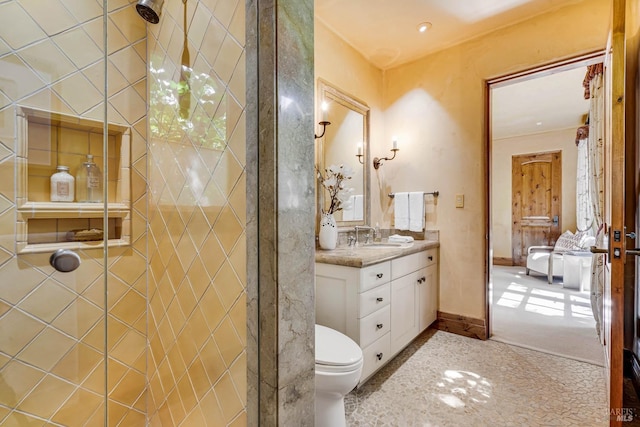bathroom with toilet, baseboards, tiled shower, and vanity