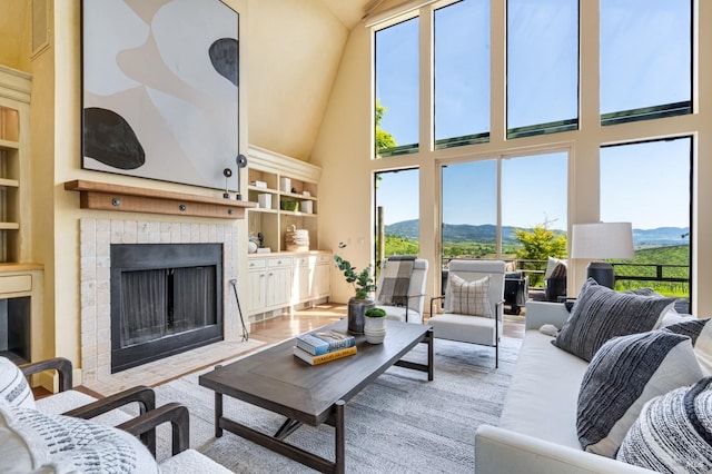 living room featuring high vaulted ceiling, a mountain view, a tiled fireplace, and plenty of natural light