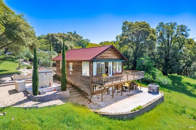 rear view of house with a lawn, a deck, metal roof, and a patio area