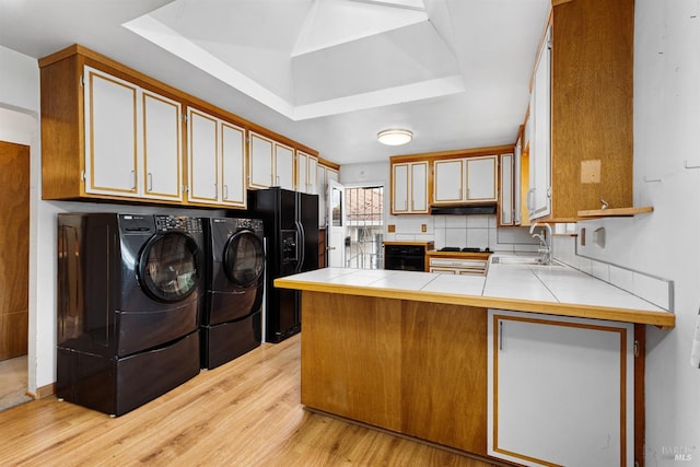 kitchen with a peninsula, washer and dryer, light wood-type flooring, a sink, and black fridge