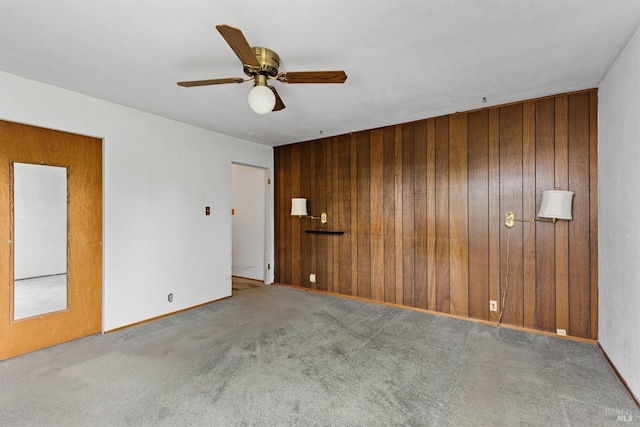 empty room featuring wooden walls, a ceiling fan, and carpet floors
