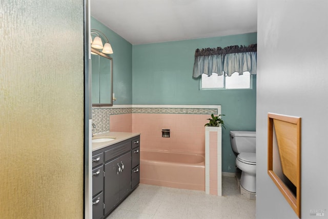 bathroom featuring a garden tub, vanity, toilet, speckled floor, and a wainscoted wall