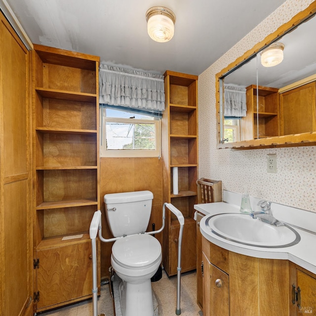 bathroom featuring toilet, wallpapered walls, and vanity