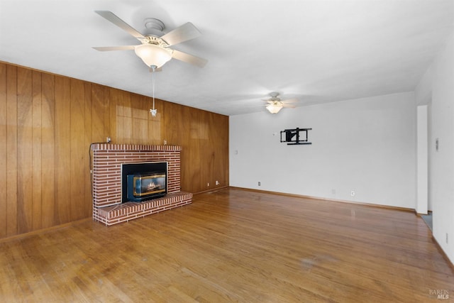 unfurnished living room with baseboards, a fireplace, a ceiling fan, and wood finished floors