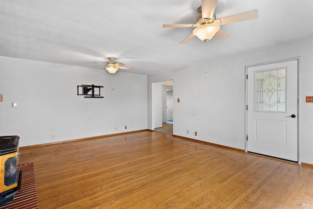 unfurnished living room featuring baseboards, ceiling fan, wood finished floors, and a wood stove