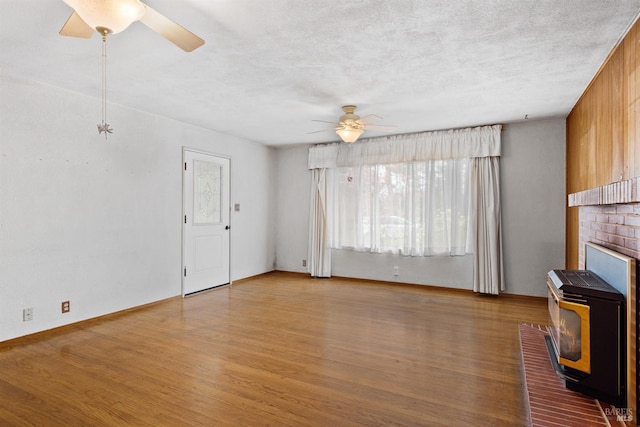 unfurnished living room featuring a wood stove, heating unit, wood finished floors, ceiling fan, and a textured ceiling