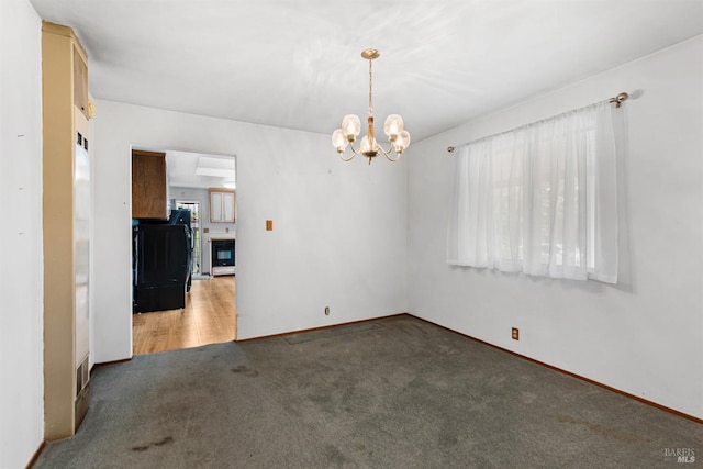 carpeted empty room featuring baseboards and an inviting chandelier