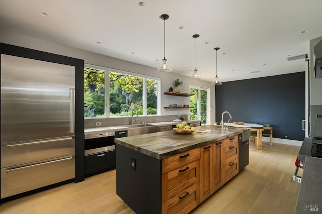 kitchen with a sink, an island with sink, light wood-type flooring, and built in fridge