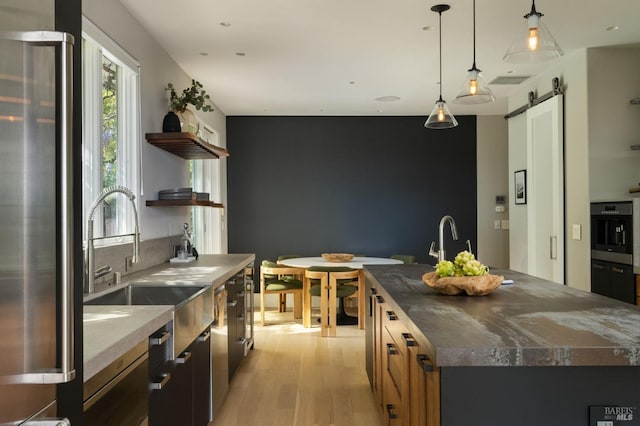 kitchen featuring open shelves, a barn door, a sink, light wood-style floors, and oven