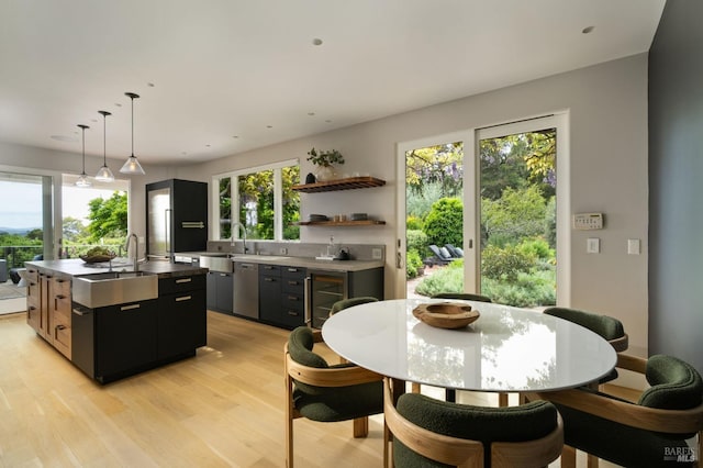 kitchen featuring stainless steel dishwasher, light wood-style floors, a center island, dark cabinetry, and a sink