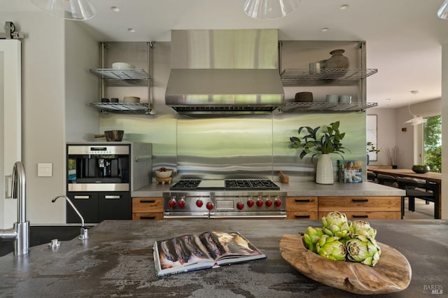 kitchen featuring wall chimney range hood, dark stone counters, stainless steel appliances, and a sink