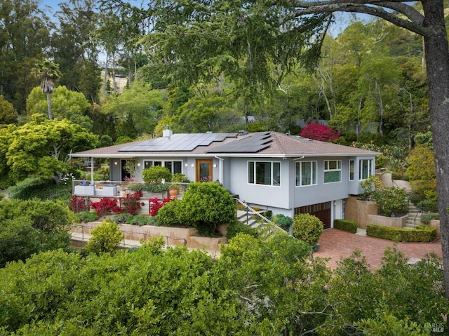 view of front of property featuring an attached garage, stucco siding, roof mounted solar panels, a chimney, and decorative driveway