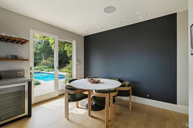dining room featuring light wood-style floors, a dry bar, baseboards, and beverage cooler