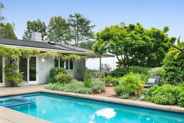 rear view of property featuring stucco siding, a pool with connected hot tub, and a chimney