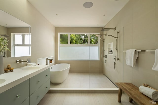 full bathroom with double vanity, a walk in shower, a freestanding tub, and a sink