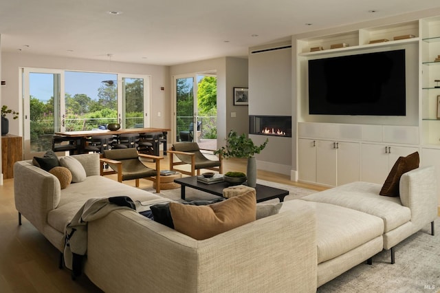 living area featuring baseboards, light wood-type flooring, and a warm lit fireplace