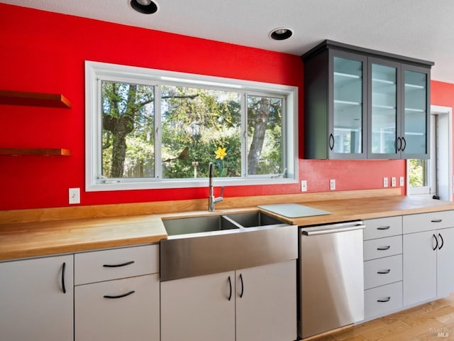 kitchen featuring stainless steel dishwasher, a sink, glass insert cabinets, and butcher block counters