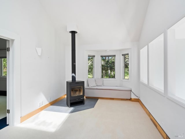 unfurnished living room featuring carpet floors, baseboards, a wood stove, and lofted ceiling
